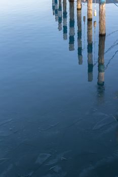 Wooden piers reflexes on the surface of the frozen lake