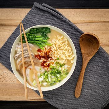 Asian ramen noodle pork bone based soup with pork chashu on cutting board background.
