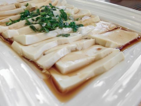 Plate of tofu slices with parsley, onions and soy sauce. Shallow depth of field.