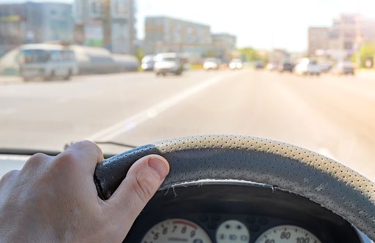 the driver hand on the steering wheel of a car that passes through a city street