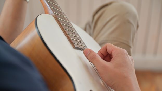 Close-up shot of a young man playing guitar at home He stopped at home because of the virus outbreak,shot from above the shoulder.