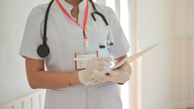 Cropped shot of Nurse wearing gloves using tablet to record covid-19 virus infected person.