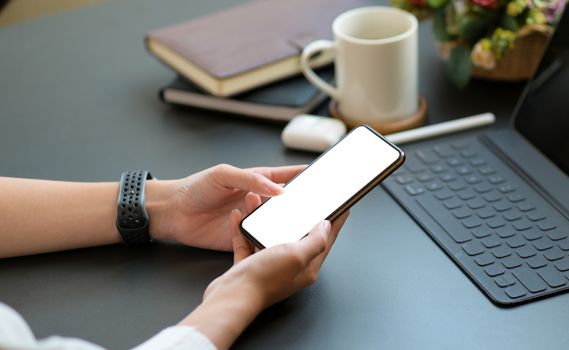 Close-up shot of a Young woman using a blank screen smartphone with a laptop and coffee on the desk.