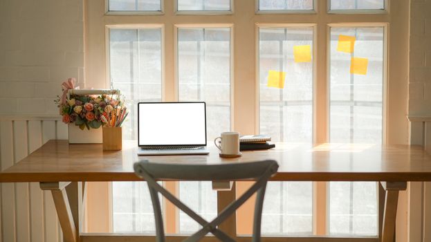 Cropped shot of classic workplace with a laptop, coffee cup and stationary on a wooden table near the window.