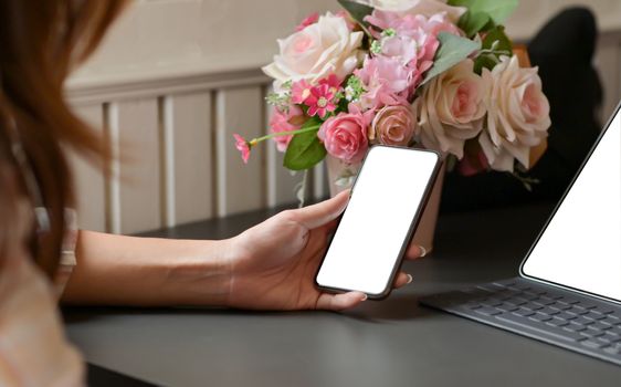 Cropped shot of A woman holding a smartphone in  hand with laptop on the desk at home office.