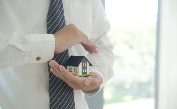 Property insurance concept: Insurance agent holds a house model in hand showing the symbol of home insurance.