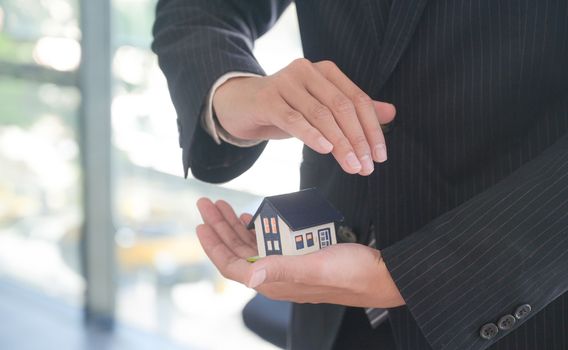 Property insurance concept: Insurance agent holds a house model in hand showing the symbol of home insurance.