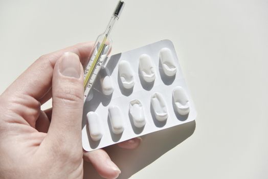 thermometer and pack of pills on the white background with the humans hand