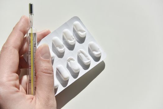 thermometer and pack of pills on the white background with the humans hand 