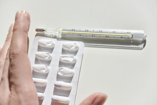 thermometer and pack of pills on the white background with the humans hand in a questioning gesture
