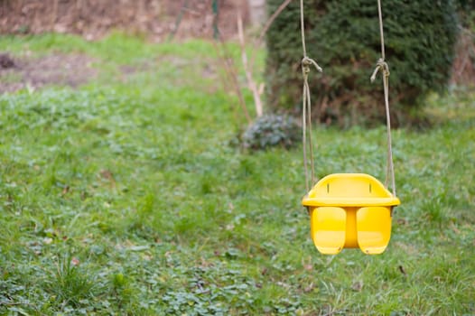 Empty yellow baby swing hanging on a tree with a grass background