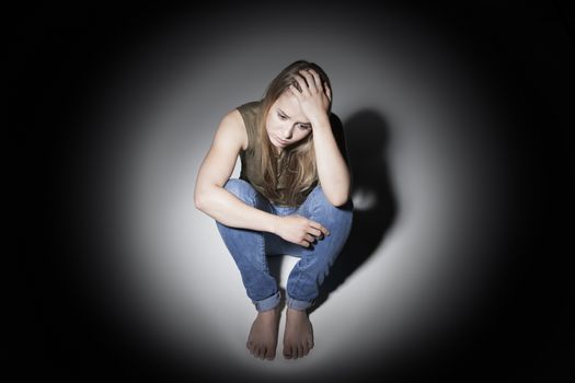 Unhappy Young Woman Sitting In Pool Of Light