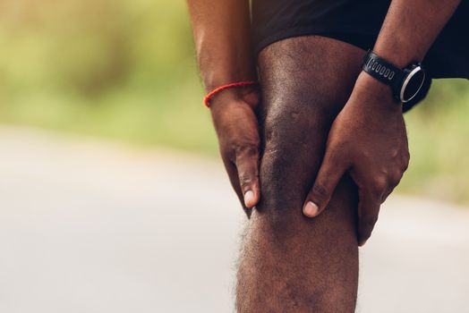 Close up Asian young sport runner black man wear watch stand use hands joint hold knee pain during the run while running at the outdoor street health park, healthy exercise injury from workout concept