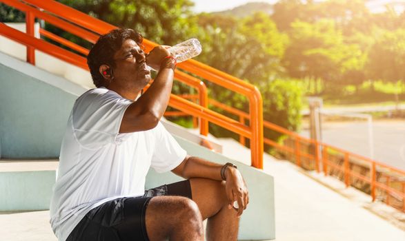 Close up Asian young sport runner black man wear athlete headphones he drinking water from a bottle after running at the outdoor street health park, healthy exercise workout concept