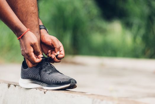 Close up Asian sport runner black man wear watch stand step on the footpath trying shoelace running shoes getting ready for jogging and run outdoor street health park, healthy exercise workout concept