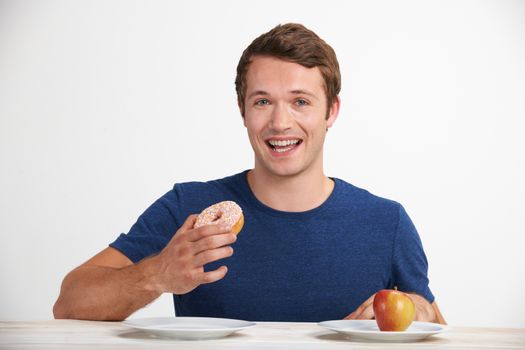 Young Man Choosing Between Doughnut And Cake For Snack