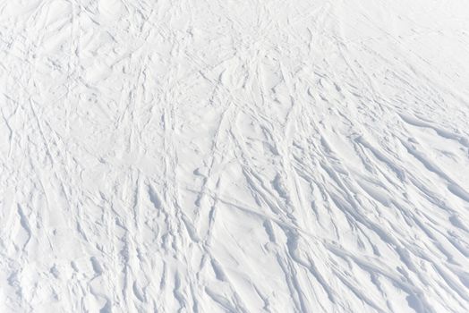 3 - gently curving linear tracks left from absent skiers cross into an intricate lattice pattern in the pure white alpine snow, background texture