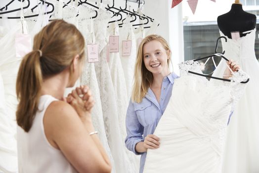 Mother Helping Daughter To Choose Dress In Bridal Store