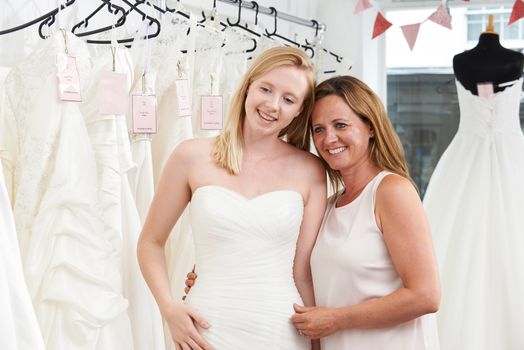 Mother Helping Daughter To Choose Dress In Bridal Store