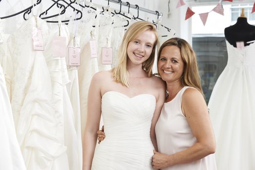 Mother Helping Daughter To Choose Dress In Bridal Store