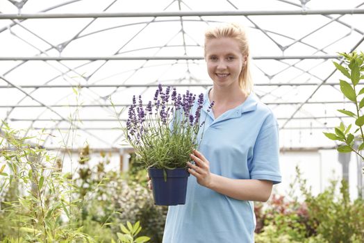 Portrait Of Female Employee At Garden Center Holding Plant