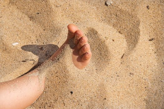 Foot in sand.  child human bare feet buried in seaside photography. Kid toe hidden in sand. Girl playing on the shore beach and hiding her barefoot. Joy and happy photo of recreation with covered legs