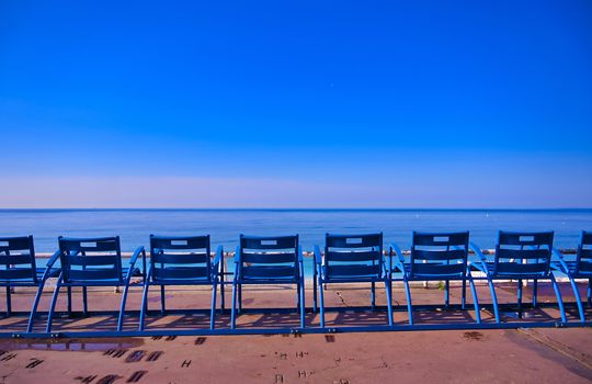 Blue chairs along the Promenade des Anglais on the Mediterranean Sea at Nice, France along the French Riviera.