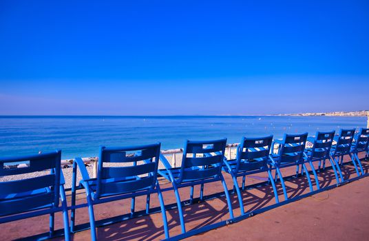 Blue chairs along the Promenade des Anglais on the Mediterranean Sea at Nice, France along the French Riviera.