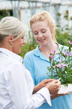 Staff Giving Plant Advice To Female Customer At Garden Center