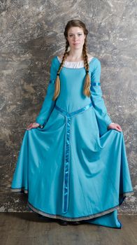 Pretty young woman in historical medieval blue dress poses in studio