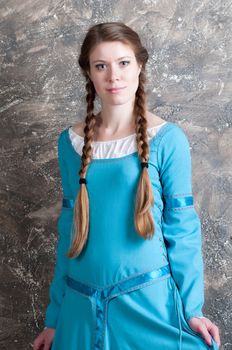 Pretty young woman in historical medieval blue dress poses in studio