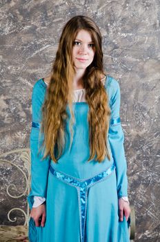 Pretty young woman in historical medieval blue dress poses in studio