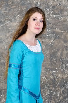 Pretty young woman in historical medieval blue dress poses in studio