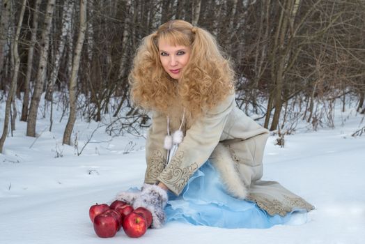 Smiling young woman with unusual hairstyle poses with apples in winter forest