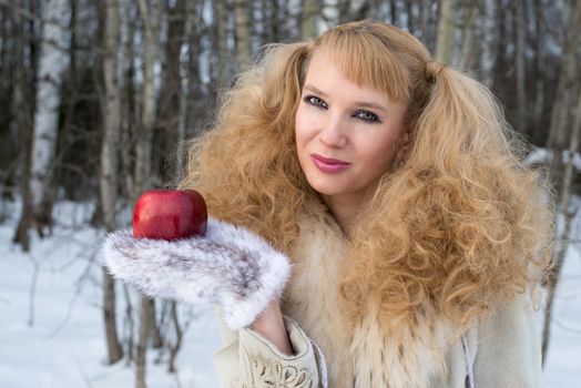 Pretty young woman with unusual hairstyle shows apple in a winter forest