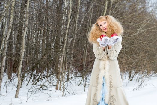 Sincerely smiling young woman in a winter forest with apples in her hands