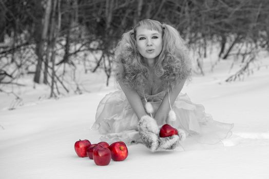 Appealing young Snow Maiden - the grandaughter of Father Frost - in transparent blue dress poses at winter forest with apples