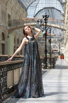 Caucasian tender young model is posing in a short black dress and lengthy transparent cape at old fashioned building with pillars