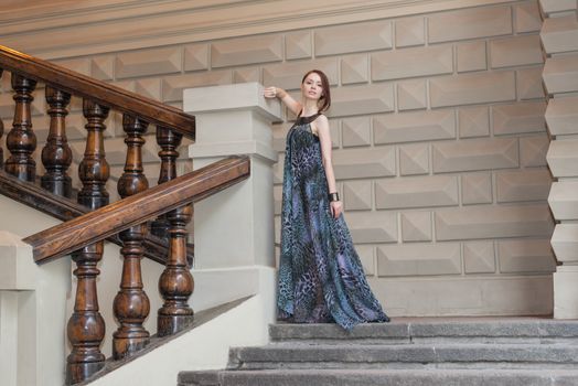 Charming lovely woman in gorgeous dress is posing on stairs of historic building