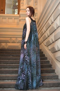 Charming lovely woman in gorgeous dress is posing on stairs of historic building