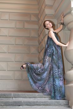 Charming lovely woman in gorgeous dress is posing on stairs of historic building