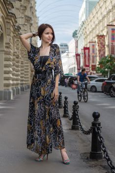 Charming sensual woman in fashionable gauzy clothing is posing at a town street with cars and people at blurred background