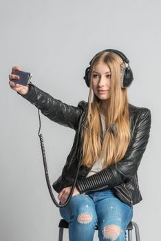 Young charming teenage girl is making selfie and listening music from personal mobile phone through wired headphones