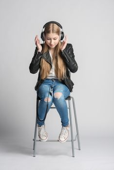 Adorable smiling girl in wired headphones is sitting and listening music from her own smartphone