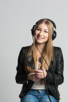 Adorable smiling girl in wired headphones is listening and enjoying music from her own smartphone