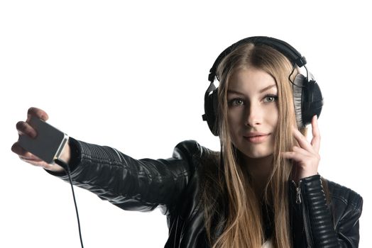 Isolated on white portrait of a young model with long hair who is making selfie and a grimace while listening music in wired headphones