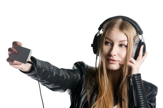 Isolated on white portrait of a young model with long hair who is making selfie and a grimace while listening music in wired headphones