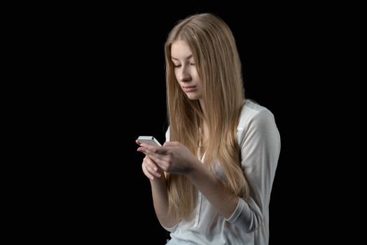 Attractive young girl feels depressed after reading bad sms on her mobile cellular phone. Isolated on black.