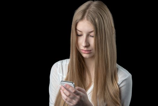 Attractive young girl feels depressed after reading bad sms on her mobile cellular phone. Isolated on black.