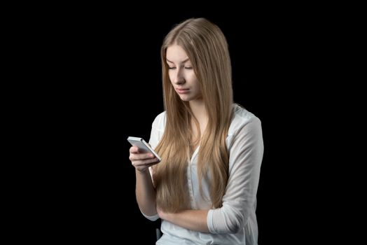 Attractive young girl feels depressed after reading bad news on her mobile cellular phone. Isolated on black.